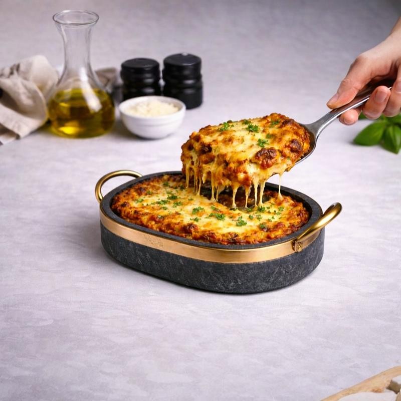 “Cheesy baked lasagna served in a handcrafted soapstone baking dish with brass handles, natural stone oven cookware for casseroles and artisan cooking.”