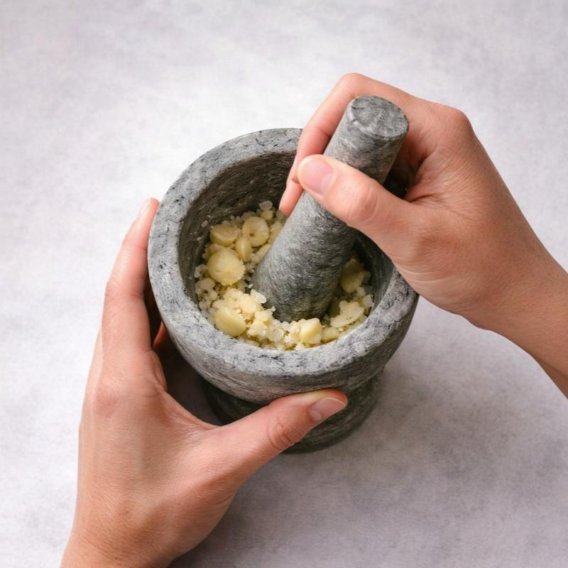 “Hand grinding garlic in a grey soapstone mortar and pestle, natural stone spice grinder for crushing herbs, garlic, and spices in a traditional kitchen.”